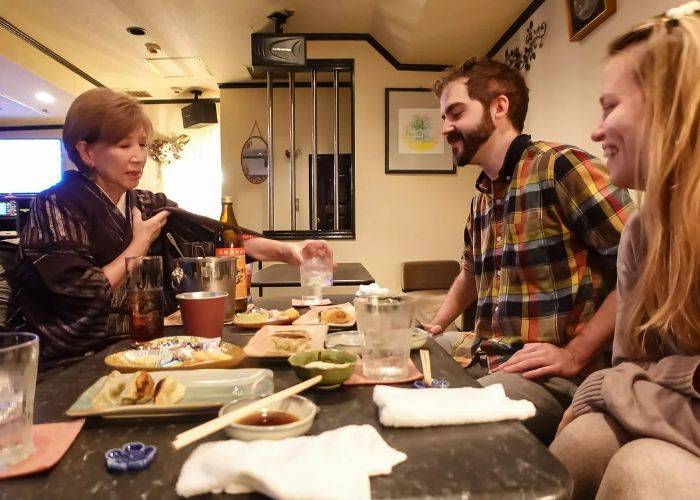 The host of a Fukuoka snack bar handing a drink to a smiling guest.